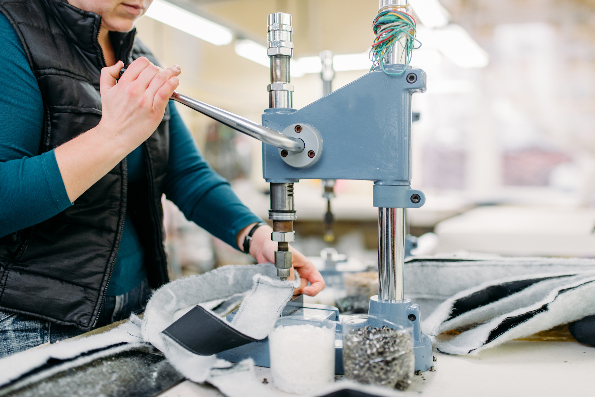 Female tailor works on riverting machine in workshop, clothing fabric. Dressmaking industry. Equipment on dress factory, professional tailoring