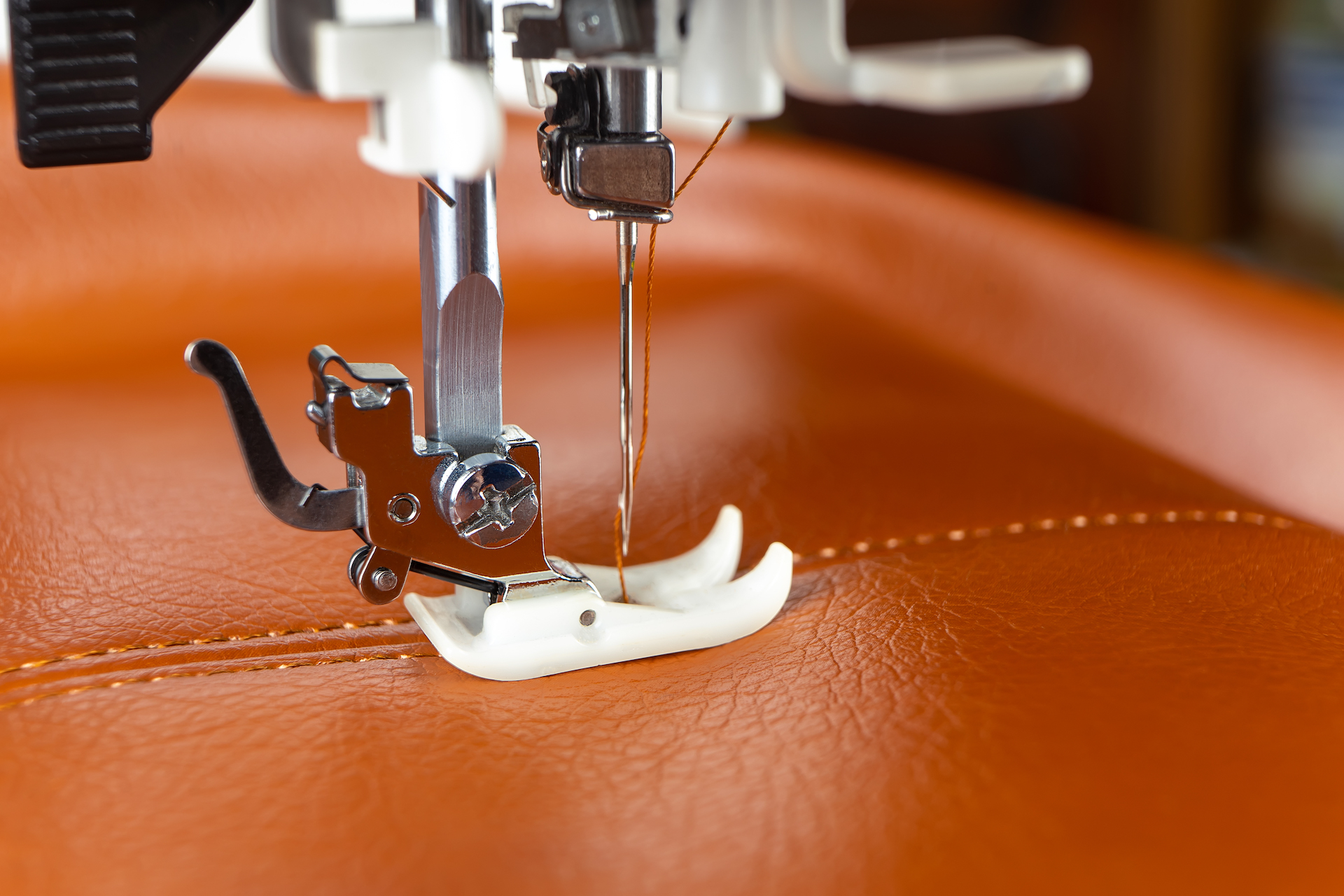 Modern sewing machine presser foot with a needle sews brown leather. Sewing process of decorative seam on leatherette with special leather presser foot. Close up, copy space.